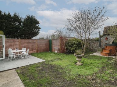 A garden with a white metal table and chairs on a patio a tree and a wooden hot tub at The Hideaway in Lympsham near Brean