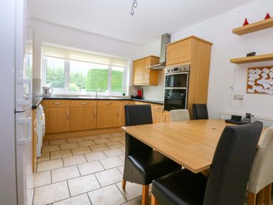 A kitchen with wooden cabinets and a table with chairs at Y Berth in Caernarfon