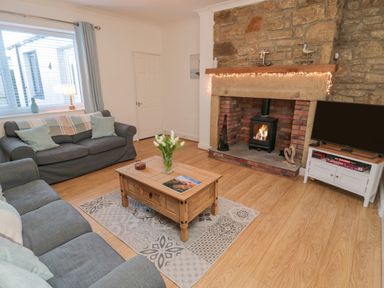 A living room with two sofas a wooden coffee table a fireplace and a television at Redshank in Amble