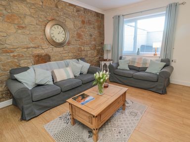 A sitting room with two grey sofas a wooden coffee table and a stone wall with a clock at Redshank in Amble
