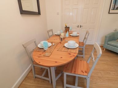 A dining table set with four place settings and chairs in a room with wooden flooring at Redshank in Amble