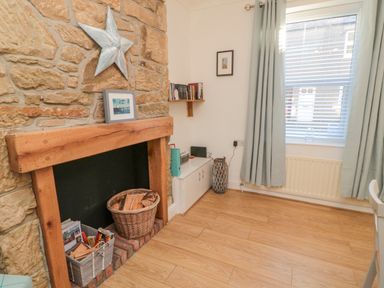 A room with a stone fireplace containing firewood baskets a window with curtains and a radiator at Redshank in Amble
