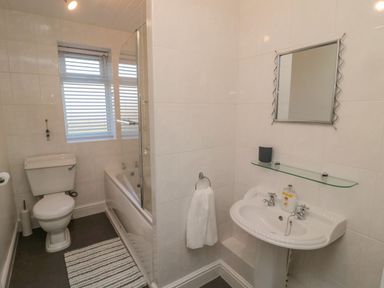 A bathroom with a toilet bathtub with shower screen sink with mirror and towel at Redshank in Amble