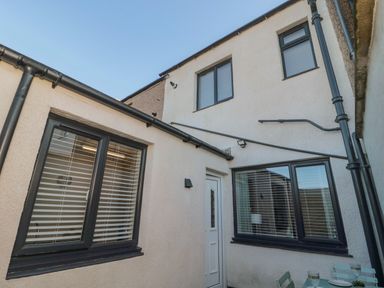 An exterior view of a building with windows and a door opening to a small outdoor seating area at Redshank in Amble