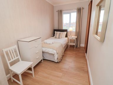 A small bedroom with a single bed, bedside table with lamp, chest of drawers, chair, and a window at Redshank in Amble
