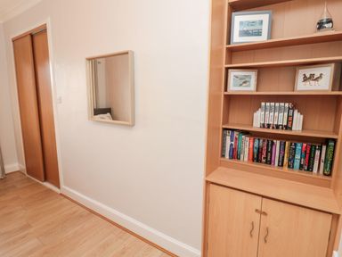 A bookshelf with books and framed pictures next to a wall mirror and wooden sliding door at Redshank in Amble