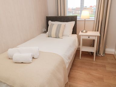 A single bed with white and striped pillows next to a white bedside table with a lamp in a bedroom at Redshank in Amble