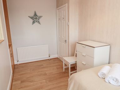 A bedroom with a white chest of drawers a white chair rolled towels on a bed a radiator and a decorative star on the wall at Redshank in Amble