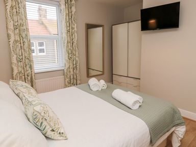 A bedroom with a bed with white and green bedding a wall mirror a wardrobe and a wall mounted TV at Redshank in Amble