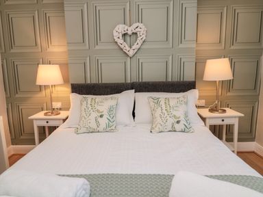 A bedroom with a double bed two bedside tables with lamps and a heart decoration on the wall at Redshank in Amble