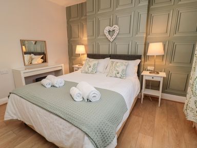 A bedroom with a double bed white bedding and rolled towels on a green throw with bedside tables and lamps at Redshank Amble