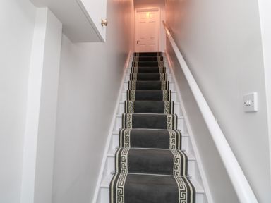 A staircase with a dark runner carpet on white stairs and a white door at the top at Redshank in Amble