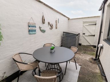 A small outdoor patio with a round table and four chairs and beach-themed wall decorations at Redshank in Amble