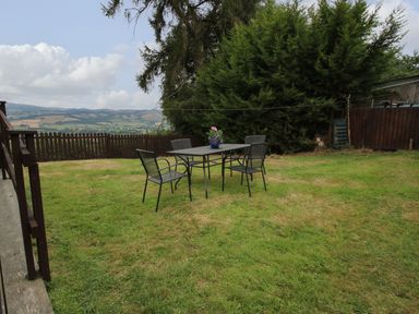 A garden with a table and four chairs on grass near a fence and trees at Dragonfly Lodge in Worthen near Minsterley