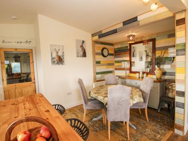 A dining area with a round table and four chairs a sideboard with a mirror and clock on a multicolored wood paneled wall at Dragonfly Lodge in Worthen near Minsterley