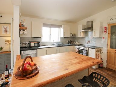A kitchen with a wooden island countertop fruit basket stove and white cabinets at Dragonfly Lodge in Worthen near Minsterley