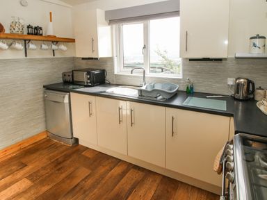 A kitchen with white cabinets black countertop a window over the sink and wooden floor at Dragonfly Lodge in Worthen near Minsterley