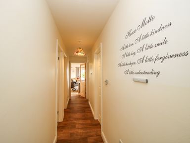 A hallway with wooden floor a pendant light on the ceiling and a wall decal with a house motto at Dragonfly Lodge in Worthen near Minsterley