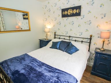 A bedroom with a double bed with blue cushions and a blanket two bedside tables with lamps and a wall mirror and moon phase artwork at Dragonfly Lodge in Worthen near Minsterley