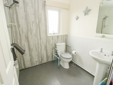 A bathroom with a toilet with safety rails a sink a shower area and a window at Dragonfly Lodge in Worthen near Minsterley