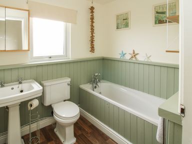 A bathroom with a sink toilet and bathtub with green wainscoting and wooden floor at Dragonfly Lodge in Worthen near Minsterley
