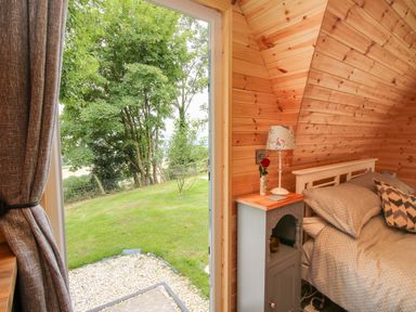 A bedroom with a bed next to a nightstand and an open door leading to a grassy outdoor area at The Pod in Worthen near Minsterley