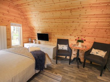 A bedroom with wooden walls two chairs a small round table a bed and a wall-mounted television at The Pod in Worthen near Minsterley