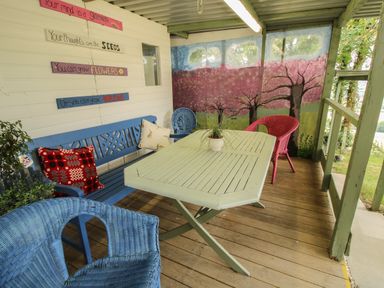 A porch with a green table surrounded by blue and red chairs and a mural of trees at The Pod in Worthen near Minsterley