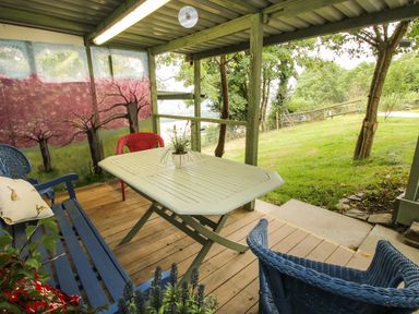 A covered outdoor seating area with a white table blue bench and chairs with a painted tree mural on the wall at The Pod in Worthen near Minsterley