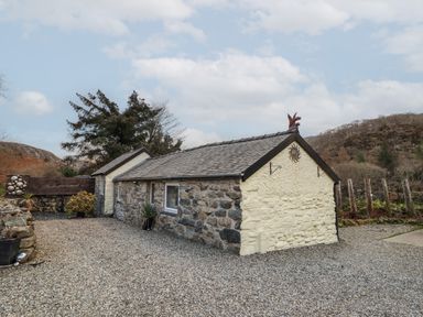 A stone cottage with a gravel driveway and plants near hills at Tyn Y Cefn Near Blaenau Ffestiniog