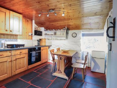 A kitchen with wooden cabinets wooden table and chairs open shelves and a small white refrigerator at Tyn Y Cefn Near Blaenau Ffestiniog