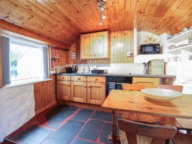 A kitchen with wooden cabinets a wooden dining table with chairs and a window at Tyn Y Cefn Near Blaenau Ffestiniog