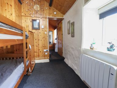 A small bedroom with wooden bunk beds a wooden wardrobe and a heater under a window at Tyn Y Cefn Near Blaenau Ffestiniog