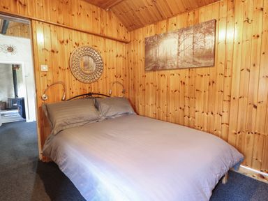 A bedroom with a double bed gray bedding wooden paneled walls and a round mirror near the door at Tyn Y Cefn Near Blaenau Ffestiniog