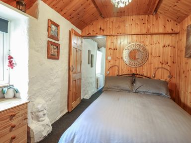 A bedroom with a double bed with grey bedding wooden wall paneling and a doorway at Tyn Y Cefn Near Blaenau Ffestiniog