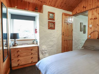A bedroom with a wooden dresser under a window and a bed with gray bedding at Tyn Y Cefn Near Blaenau Ffestiniog