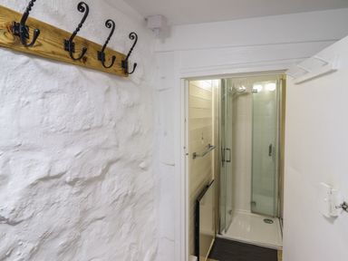 A narrow hallway with coat hooks on the wall leading to a shower with glass doors at Tyn Y Cefn Near Blaenau Ffestiniog