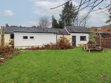 A backyard with green grass a wooden picnic table and a house with white and yellow walls near Blaenau Ffestiniog