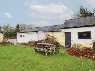 A small building with a slate roof and white and yellow walls next to a wooden picnic table on a grassy lawn at Tyn Y Cefn Near Blaenau Ffestiniog