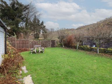 A fenced garden with a picnic table and benches near a shed with trees and hills beyond at Tyn Y Cefn Near Blaenau Ffestiniog