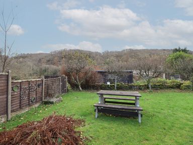 A garden with a wooden picnic table and benches surrounded by trees and a wooden fence at Tyn Y Cefn Near Blaenau Ffestiniog