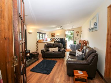 A living room with two leather sofas a small black rug a wood burning stove and a kitchen area at The Retreat in Pedairffordd near Llanrhaeadr-Ym-Mochnant