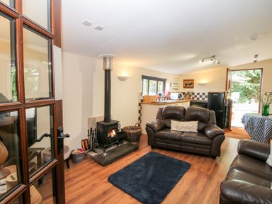A living room with leather sofas a wood burning stove and a kitchen area visible at The Retreat in Pedairffordd near Llanrhaeadr-Ym-Mochnant
