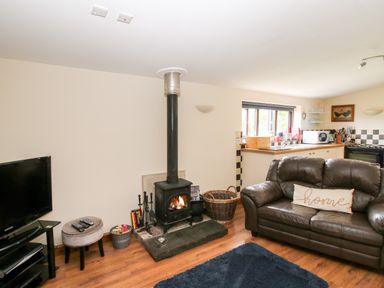 A living room with a wood stove a leather sofa with a pillow a television and an open kitchen at The Retreat in Pedairffordd near Llanrhaeadr-Ym-Mochnant