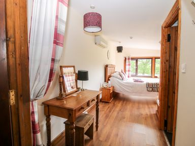 A bedroom with a wooden dressing table and stool a bed near a window and wooden flooring at The Retreat in Pedairffordd near Llanrhaeadr-Ym-Mochnant