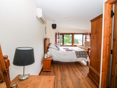 A bedroom with wooden furniture a bed with folded towels bedside table and window with plaid curtains at The Retreat in Pedairffordd near Llanrhaeadr-Ym-Mochnant