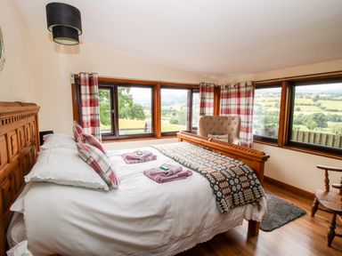 A bedroom with a bed a chair and large windows showing a countryside view at The Retreat in Pedairffordd near Llanrhaeadr-Ym-Mochnant