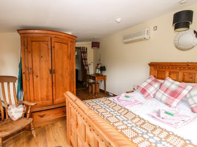 A bedroom with a wooden bed and wardrobe a wooden chair with a heart shaped pillow and a small desk with a mirror at The Retreat in Pedairffordd near Llanrhaeadr-Ym-Mochnant