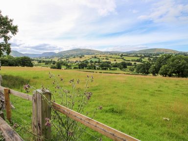 A green field with a wooden fence and hills in the background at The Retreat in Pedairffordd near Llanrhaeadr-Ym-Mochnant