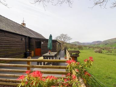 A wooden deck with a picnic table and umbrella attached to a dark wooden building overlooking green fields and hills at The Retreat in Pedairffordd near Llanrhaeadr-Ym-Mochnant